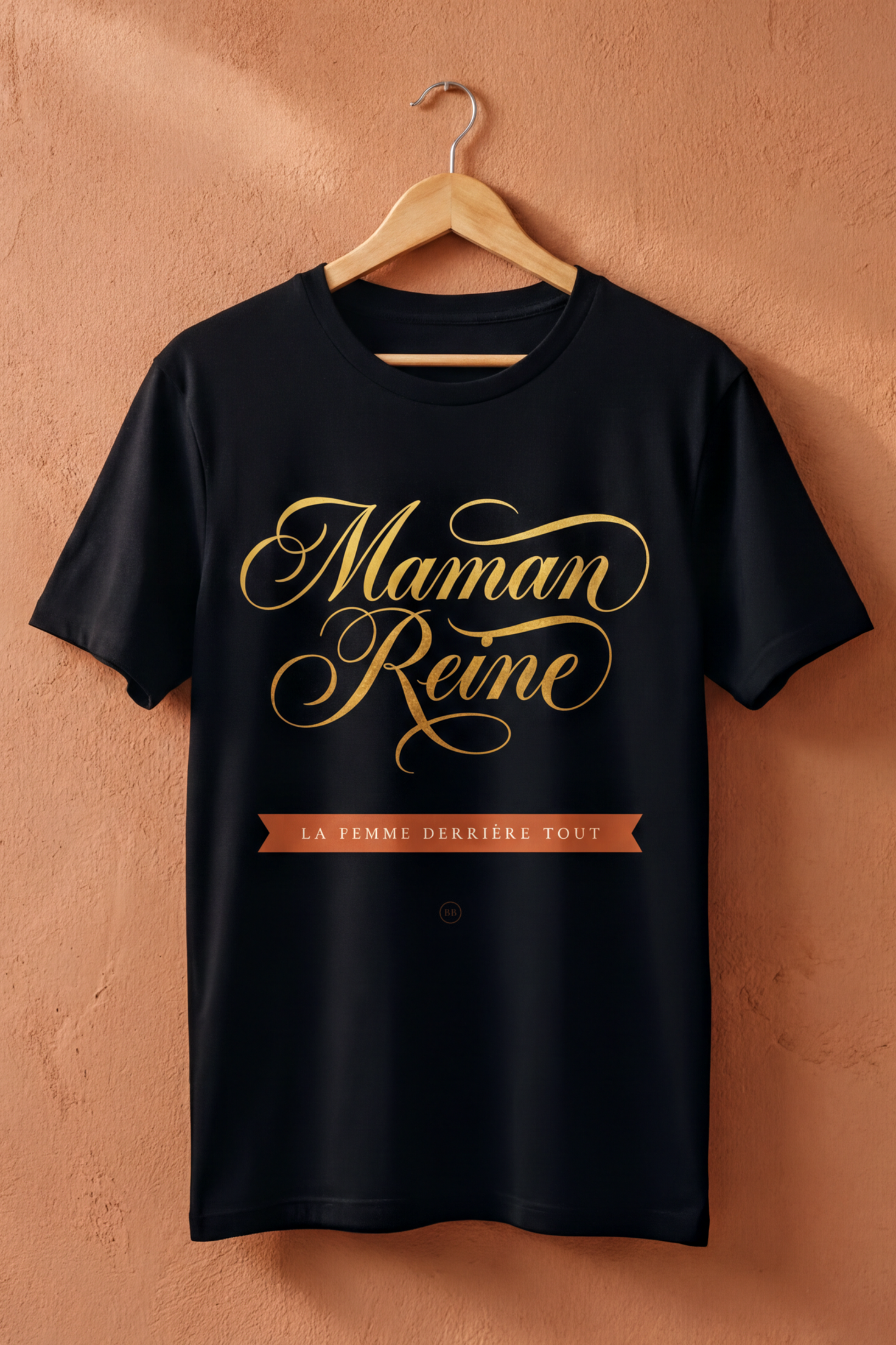Black Maman Reine tee on a wooden hanger against a terracotta wall, Essentials gift line by Bana Bilaka