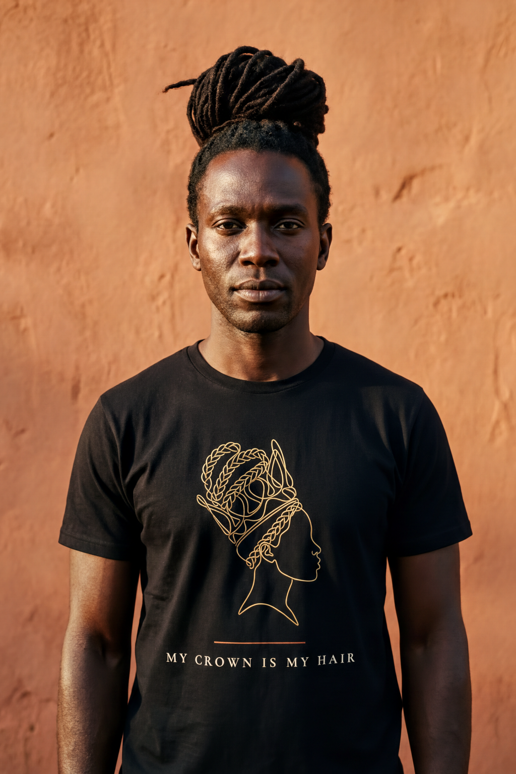 Man with long natural locs tied up high wearing the black My Crown Is My Hair tee, continuous gold line silhouette, Essentials collection by Bana Bilaka