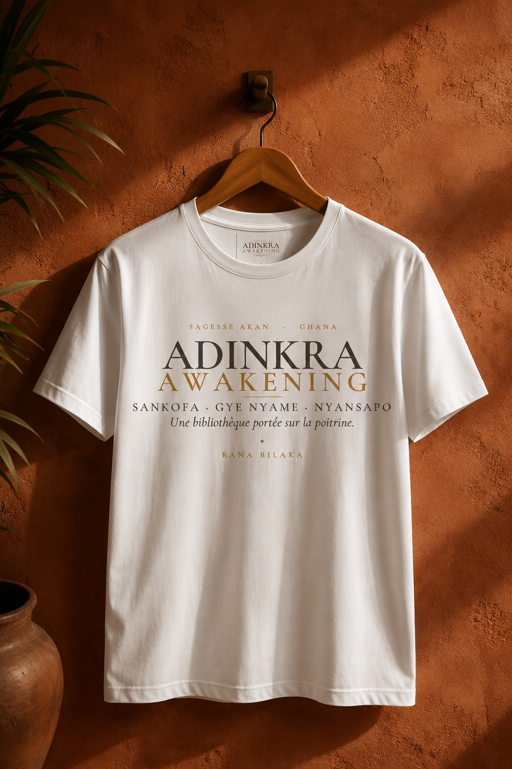 Bana Bilaka Adinkra Awakening — t-shirt blanc sur cintre, ambiance boutique terracotta