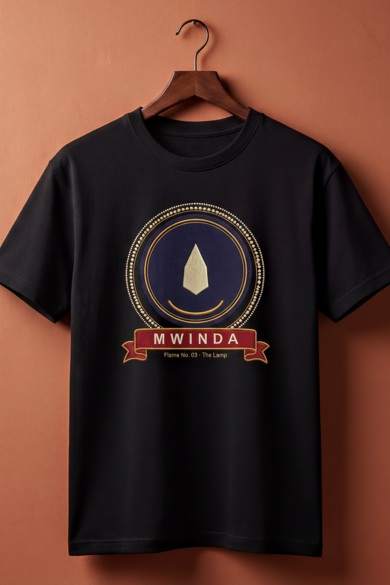 Black Mwinda tee on a wooden hanger against a terracotta wall, The Twelve Flames by Bana Bilaka