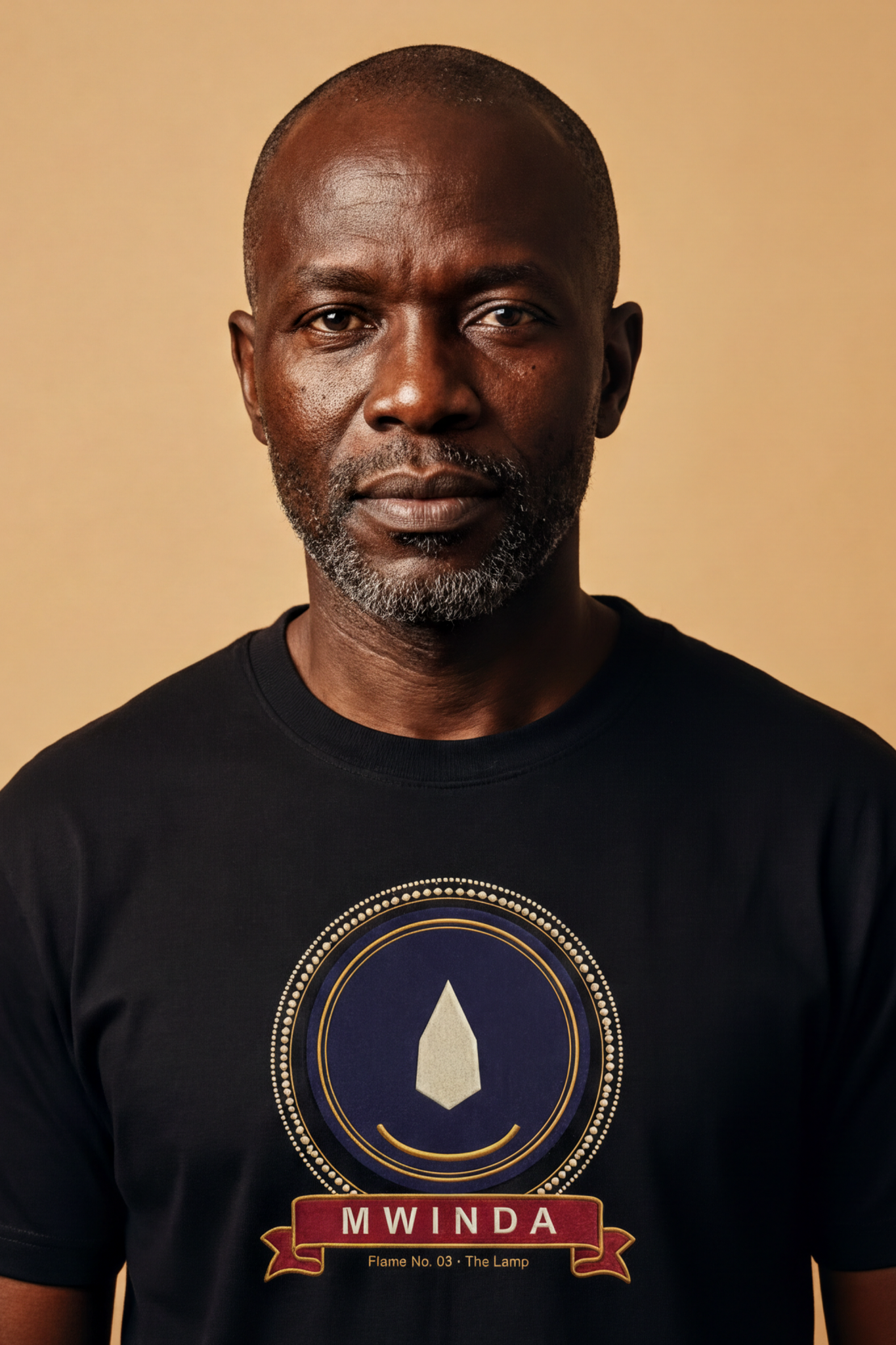 Mature man wearing the black Mwinda tee, ivory lamp flame in a gold crescent on indigo, The Twelve Flames collection by Bana Bilaka
