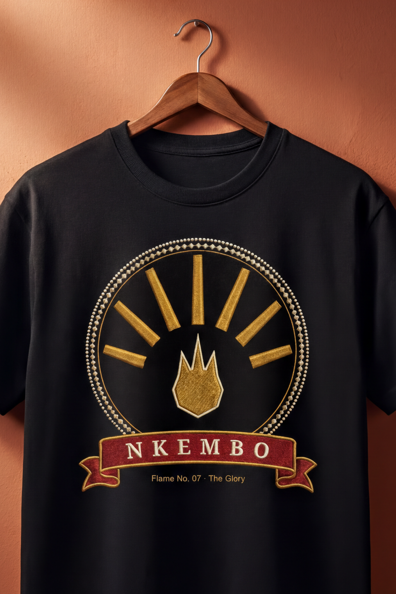 Black Nkembo tee on a wooden hanger against a terracotta wall, The Twelve Flames by Bana Bilaka