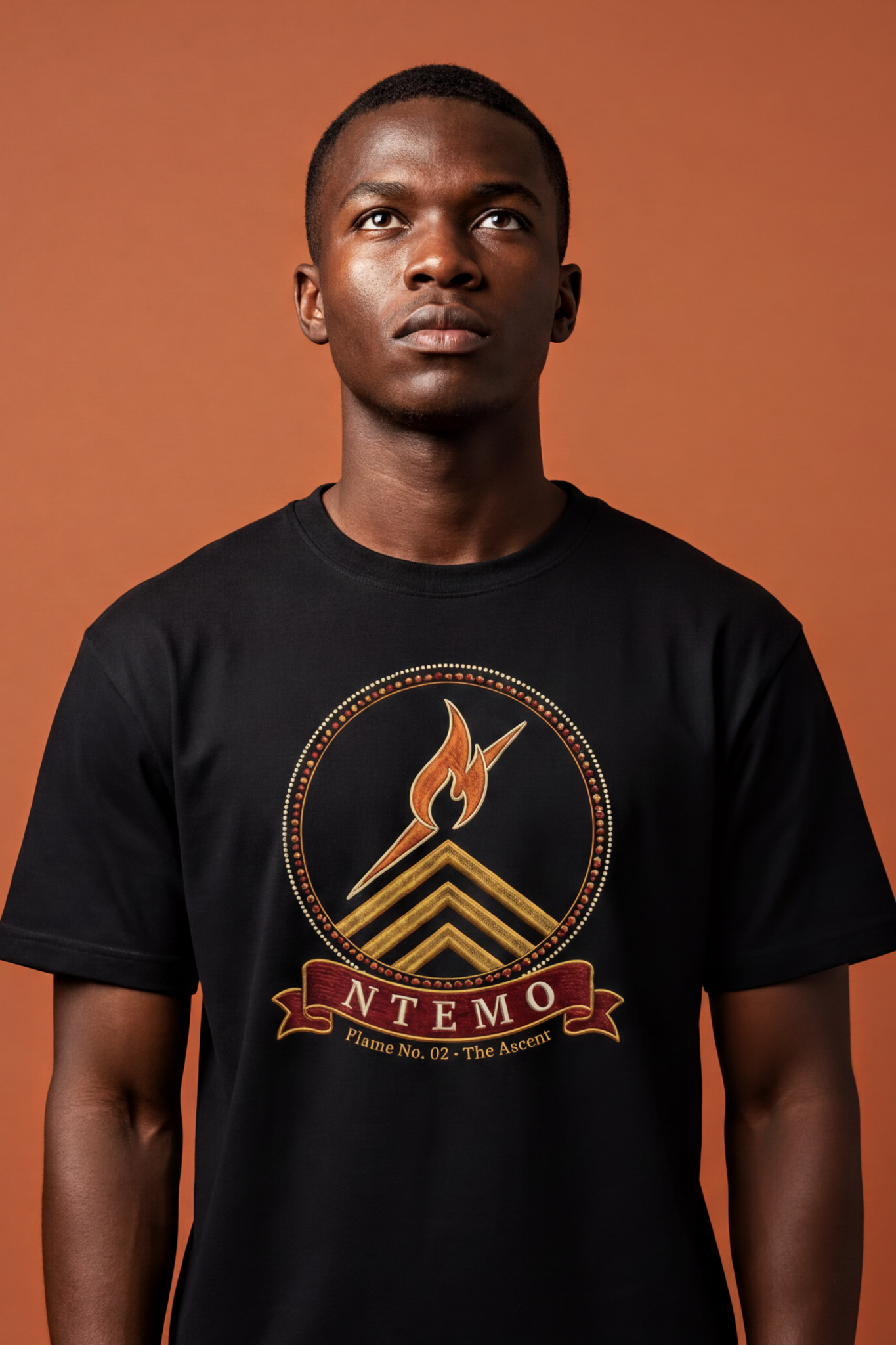 Young man wearing the black Ntemo tee, tilted dawn-orange flame over gold chevrons, The Twelve Flames collection by Bana Bilaka