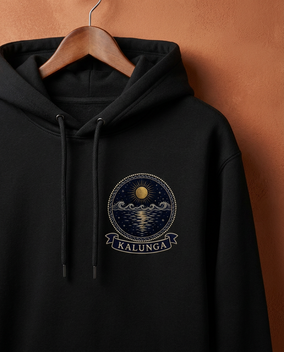 Kalunga jet black hoodie on a wooden hanger against a terracotta wall, embroidery-style Kongo Dikenga medallion (gold sun above the water line and its fragmented reflection) printed on the chest, Bana Bilaka