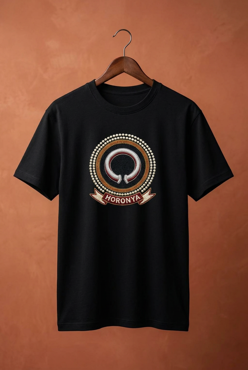 Tee noir Horonya sur cintre en bois contre un mur terracotta, imprimé effet broderie, Collection Le Serment du Manden par Bana Bilaka