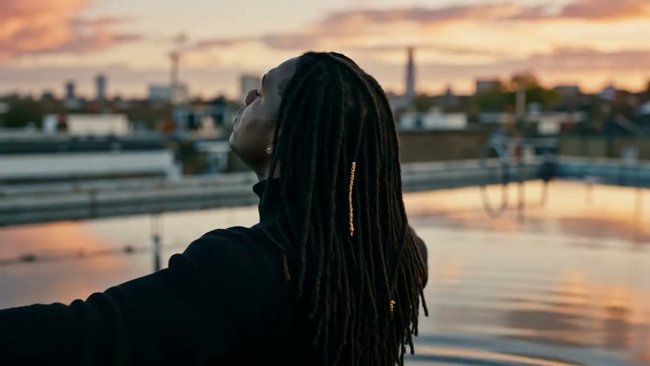 A man seen from behind, arms open on a rooftop at sunset, Quiet Crown