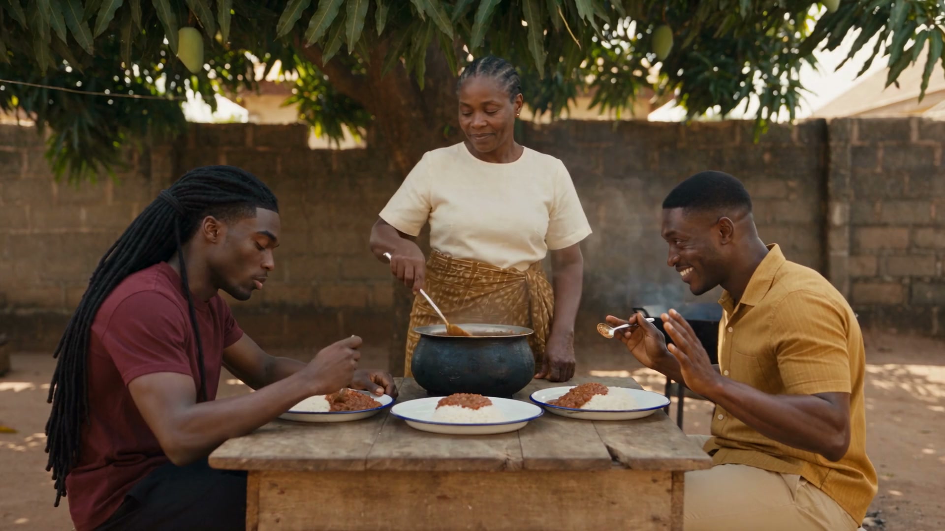 Koffi, sa mère et un ami partagent un repas autour d'une marmite sous le manguier, Koffi, les chaînes invisibles