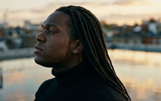Un homme de dos, bras ouverts sur un toit au coucher du soleil, Quiet Crown