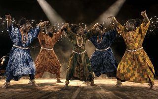 Cinq danseurs en bogolan se tiennent par la main sous les projecteurs, Quiet Crown
